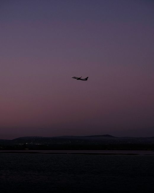 Silhouetted airplane flying over calm waters at twilight, highlighting the serene evening skyscape.