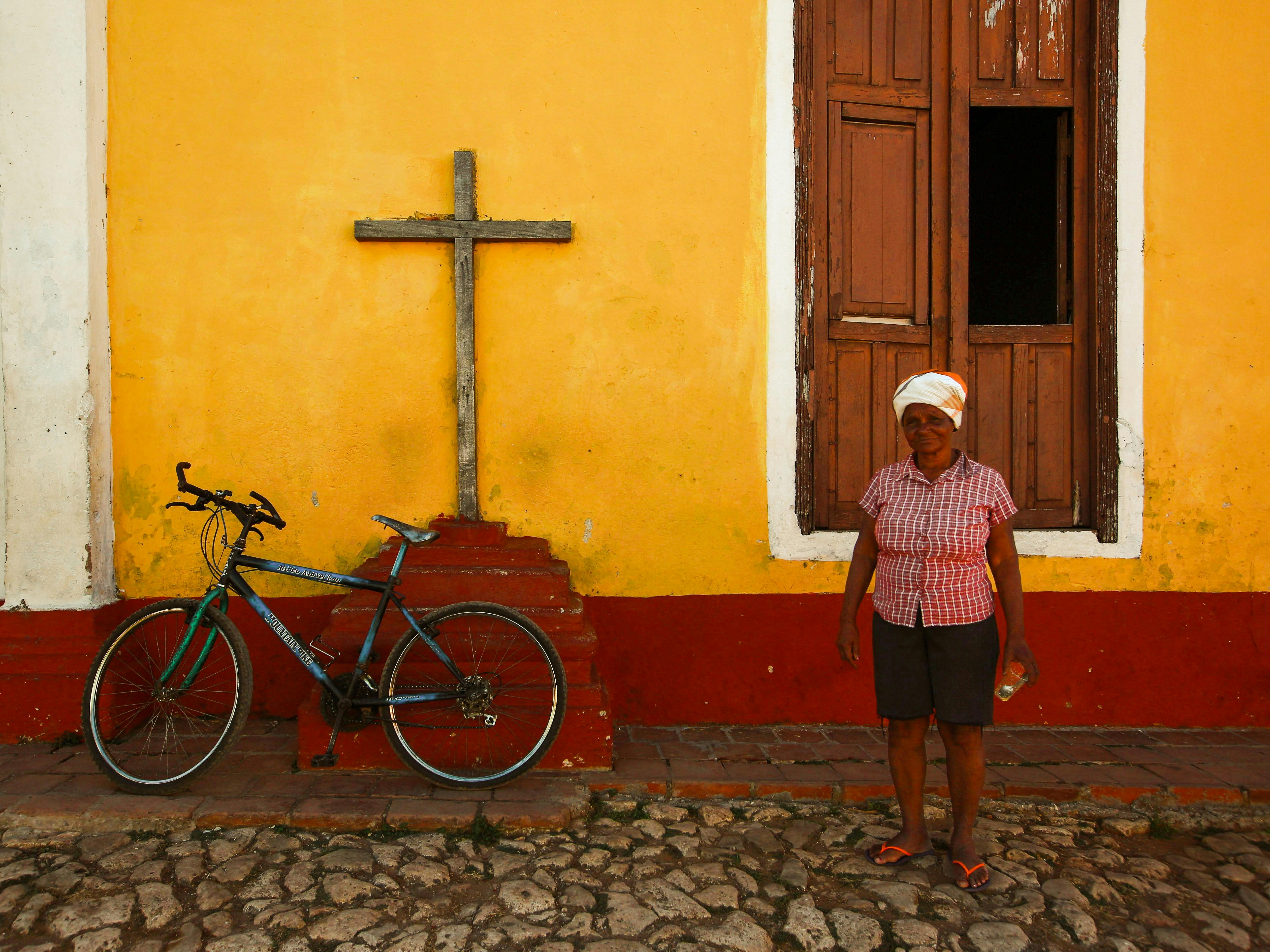 Elderly woman with bicycle near church facade on a cobblestone street.
