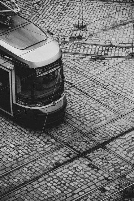 Monochrome image of a tram traversing a cobblestone street, showcasing urban transportation.