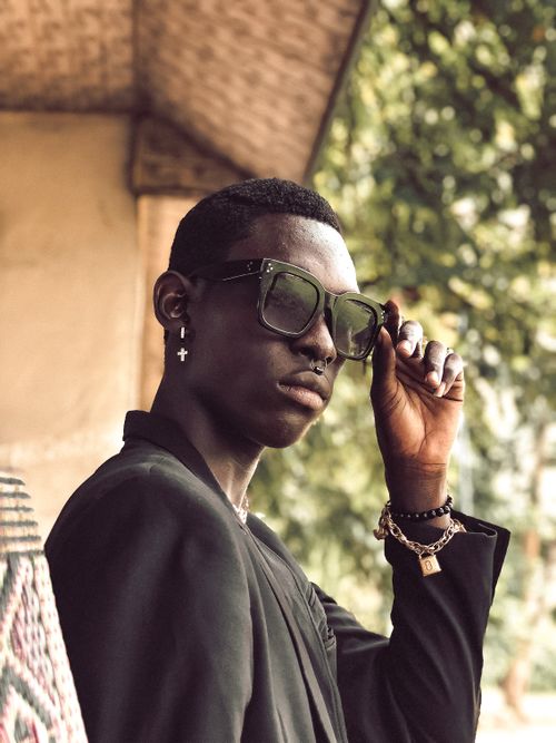 Free A fashionable man wearing sunglasses and jewelry poses confidently outdoors in a stylish portrait. Stock Photo