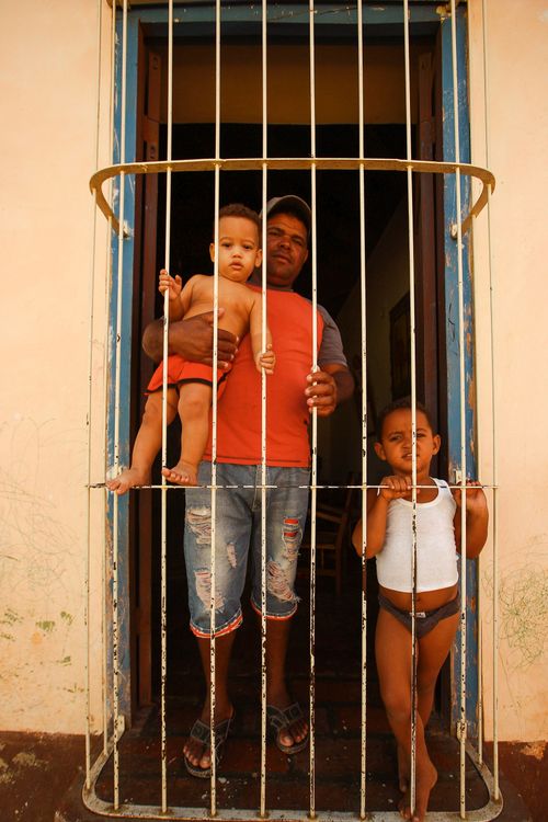 Free Father and children stand at an iron gate, looking outside from indoors. Stock Photo