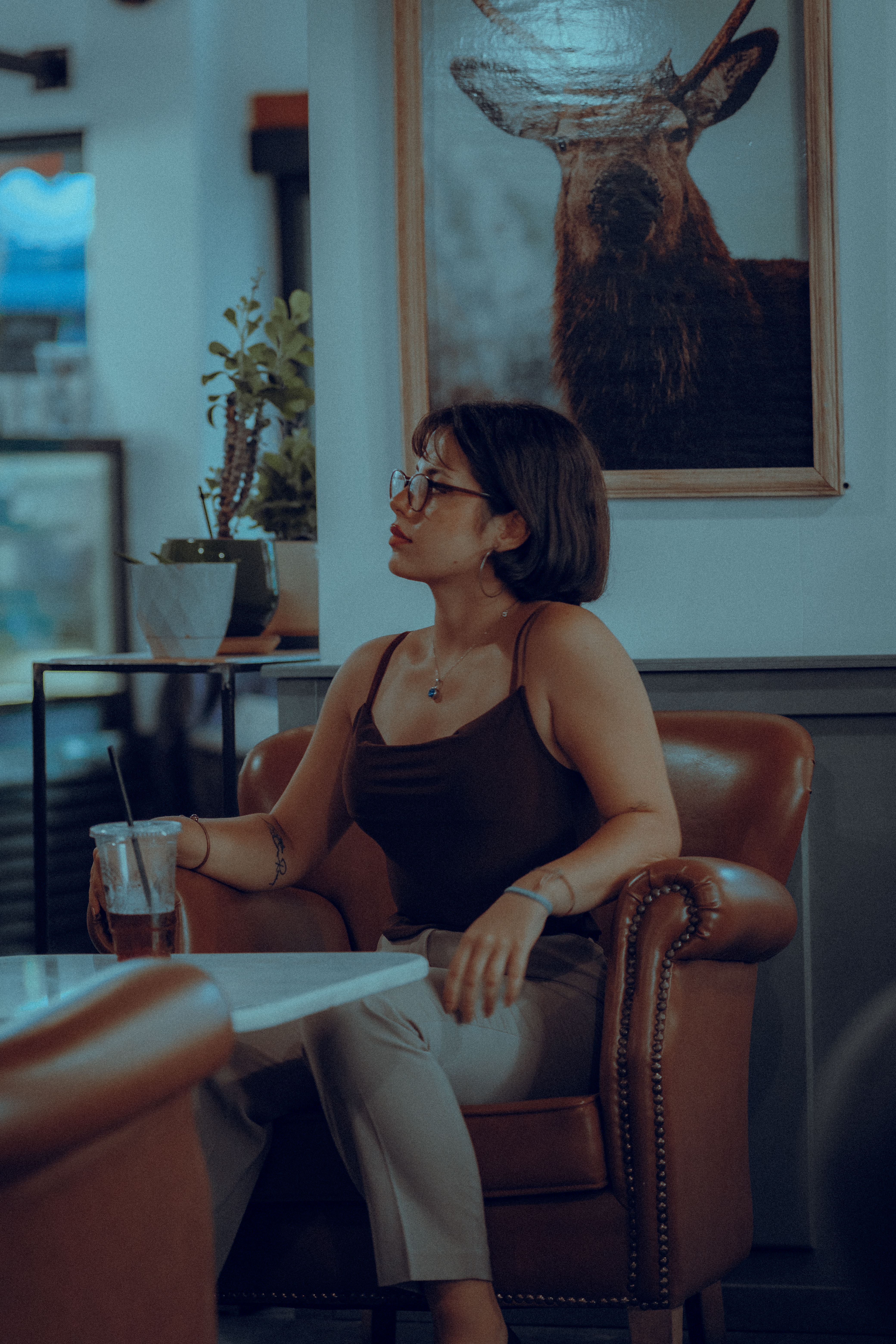 A woman with glasses enjoying a drink while sitting in a cozy armchair, indoors.