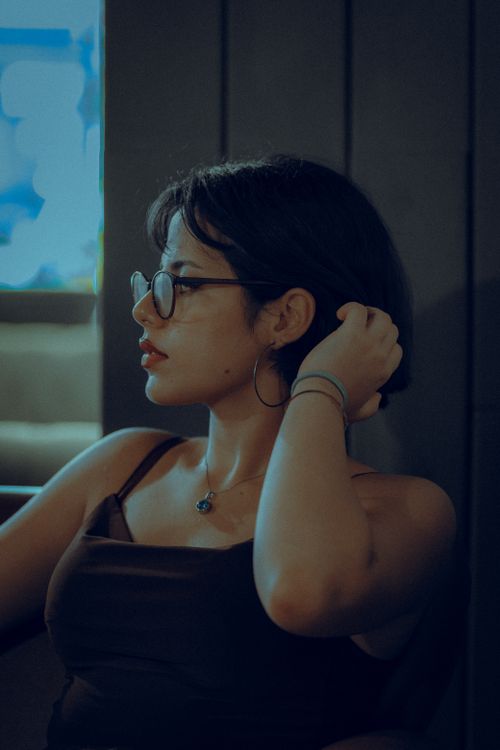 Free Profile view of a woman in glasses and necklace in moody lighting. Stock Photo