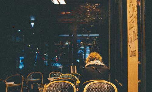 Free A solitary figure sitting in a warm, dimly lit Paris cafe during the evening. Stock Photo