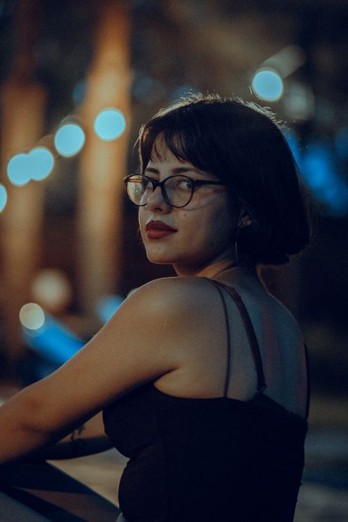 Free Stylish woman in glasses and black tank top looking back during evening outdoors. Stock Photo