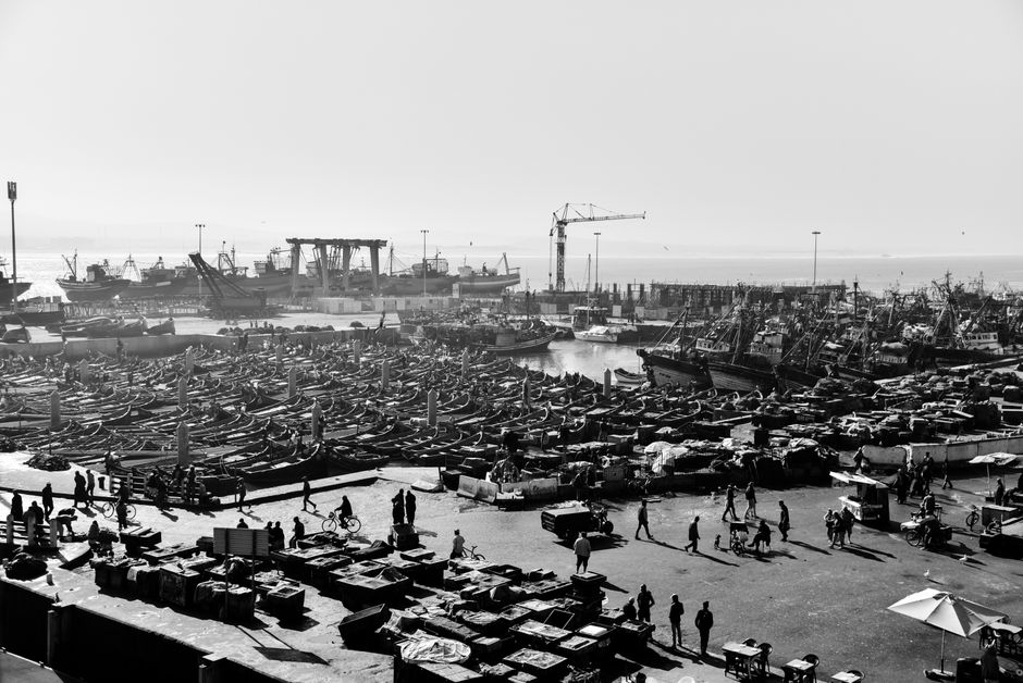 Black and white view of a busy port in Essaouira, Morocco with fishing boats and people.