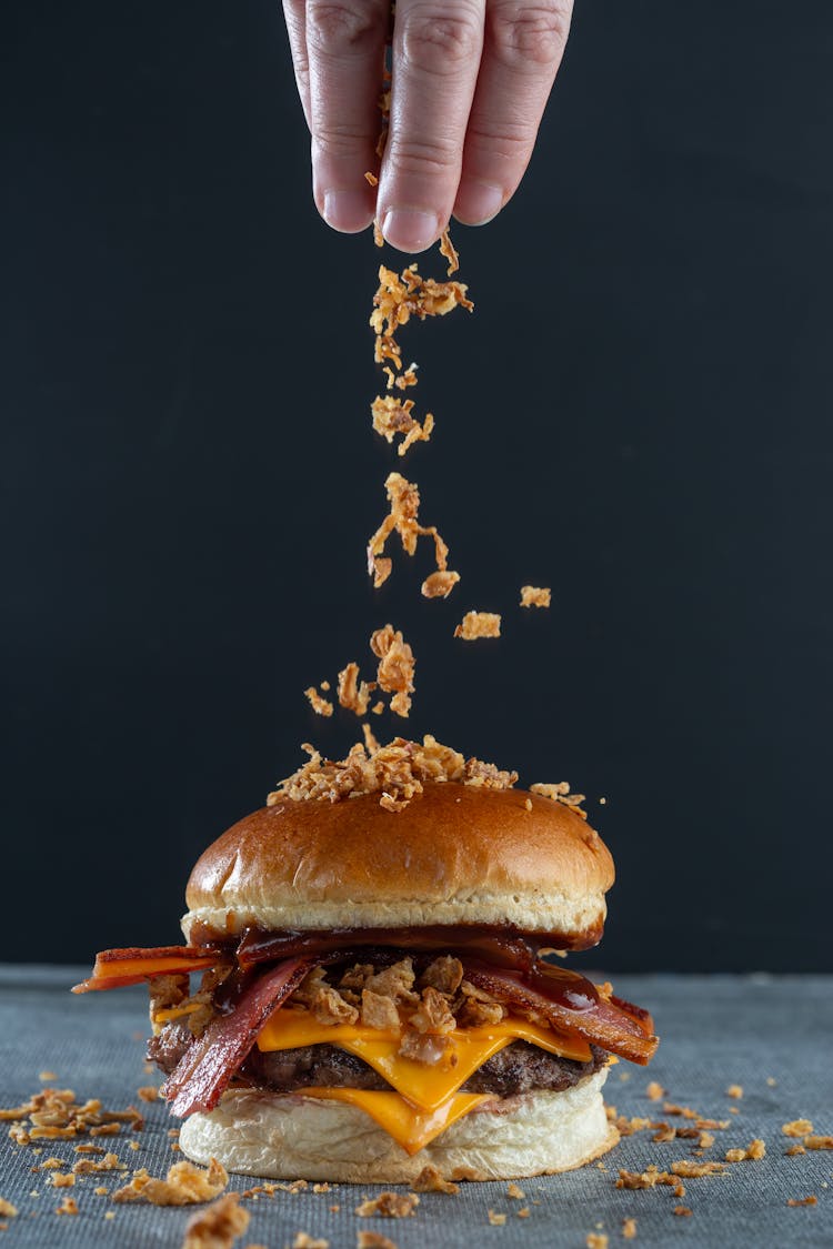 Studio Shoot Of A Hand Sprinkling A Burger