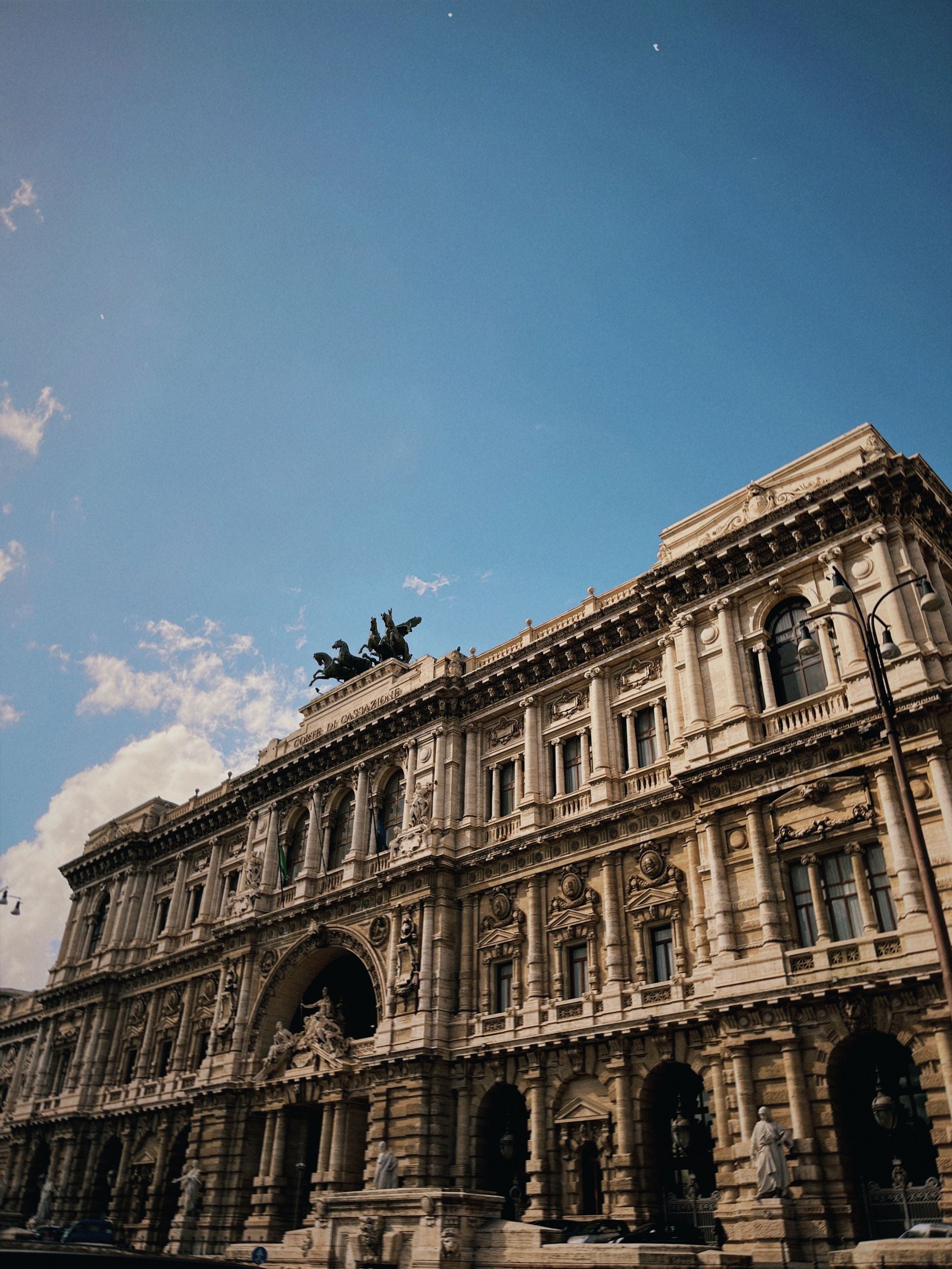 Low-angle view of a grand classical building in Rome under a vibrant blue sky.
