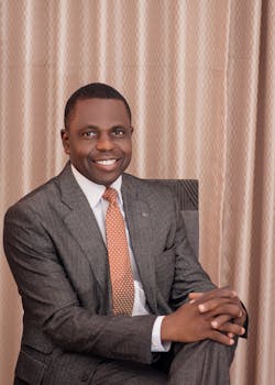Portrait of a smiling businessman in a suit and tie, sitting indoors in a formal setting.