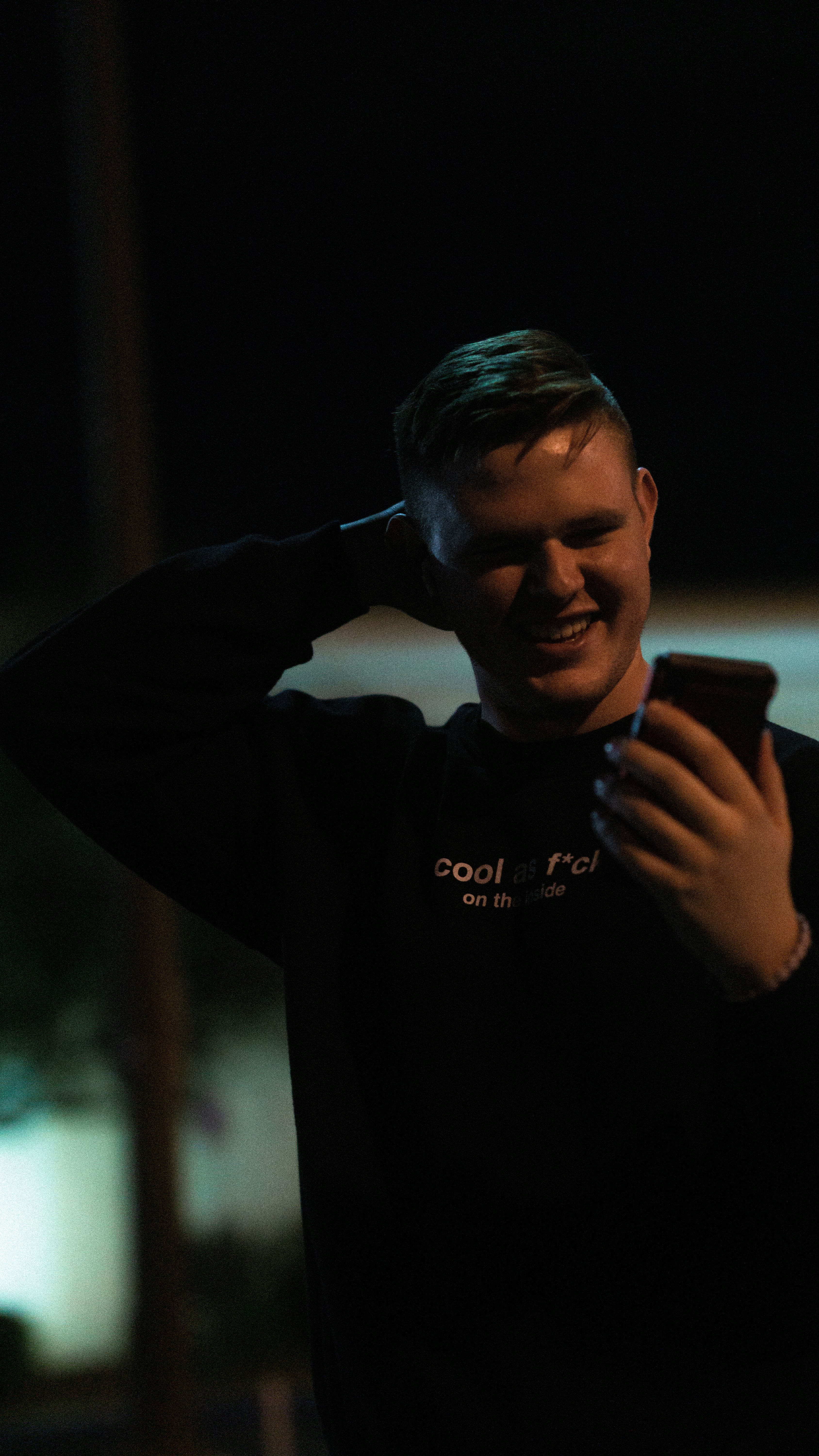 A young caucasian man smiling while using his smartphone outdoors at night.