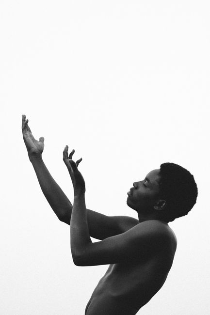 Artistic black and white portrait of a man with hands raised against a white background.