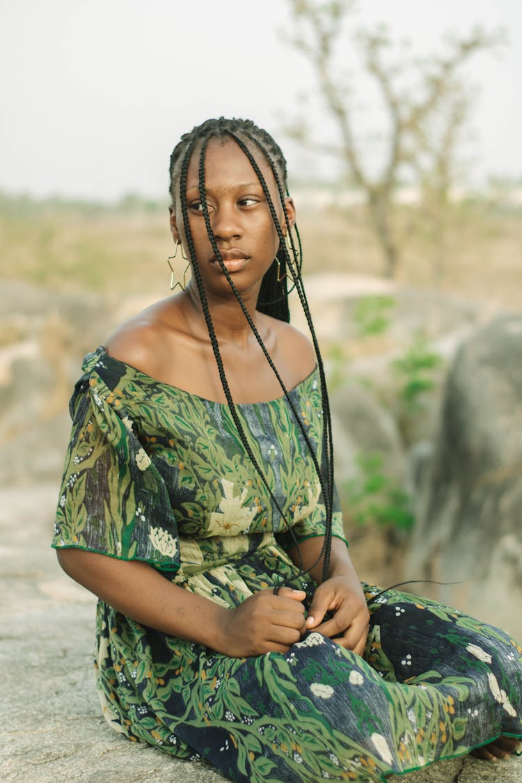 Woman In Floral Dress And Long Box Braids Sitting On Rock