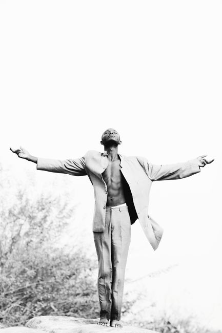 A man standing with open arms, looking up, in a spiritual black and white scene.