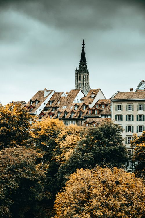 Free Stunning view of Berne with a Gothic cathedral rising above autumn foliage and historic buildings. Stock Photo