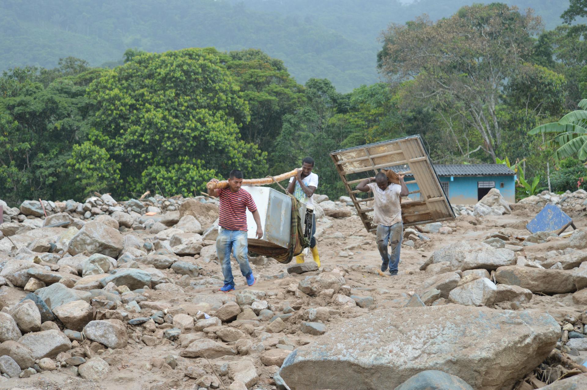 Men carrying debris through rocky terrain in rural Mocoa, Colombia after a natural disaster.