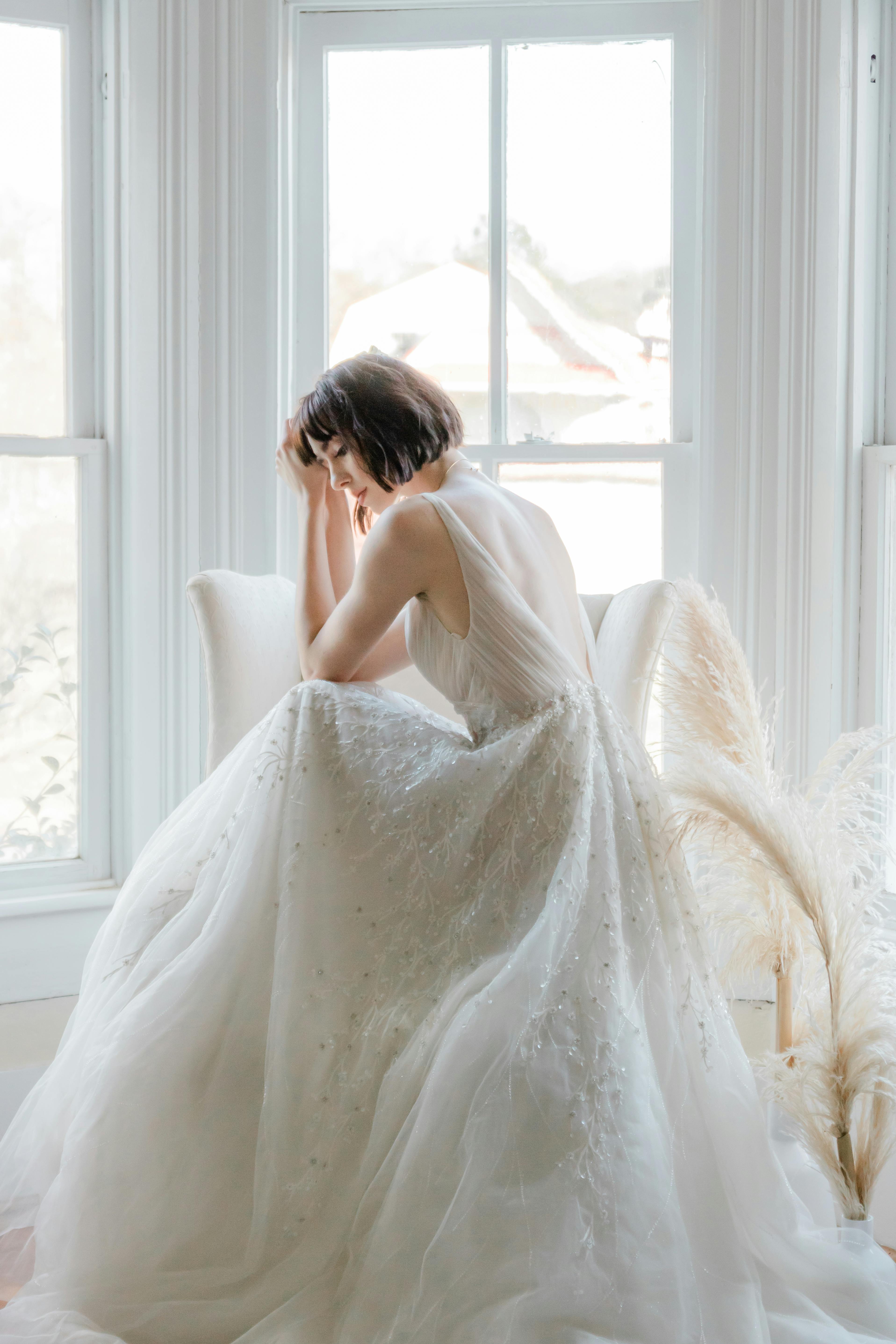 A serene bridal portrait featuring a woman sitting gracefully by a sunlit window.