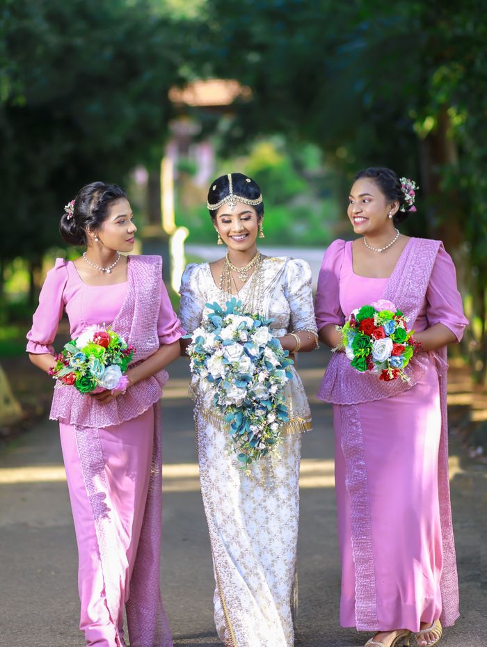 Kandyan bride walking arm-in-arm with bridesmaids in pink osariya
