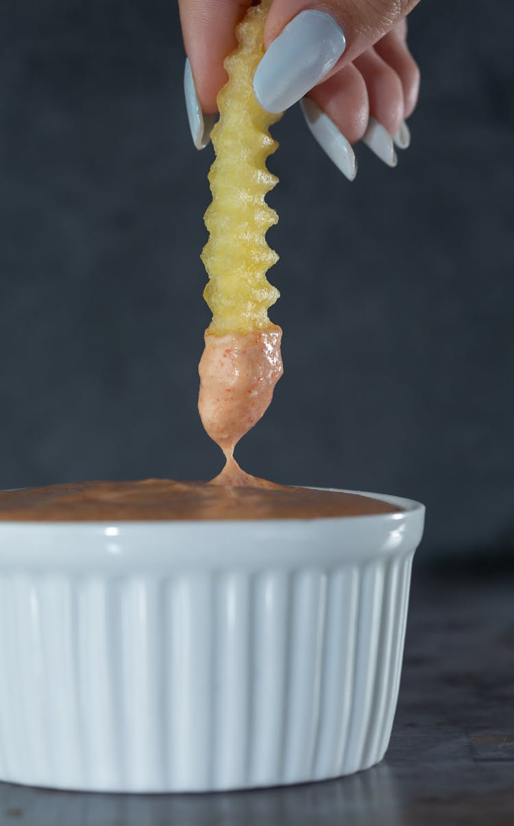 Woman Hand Dipping Fries In Sauce