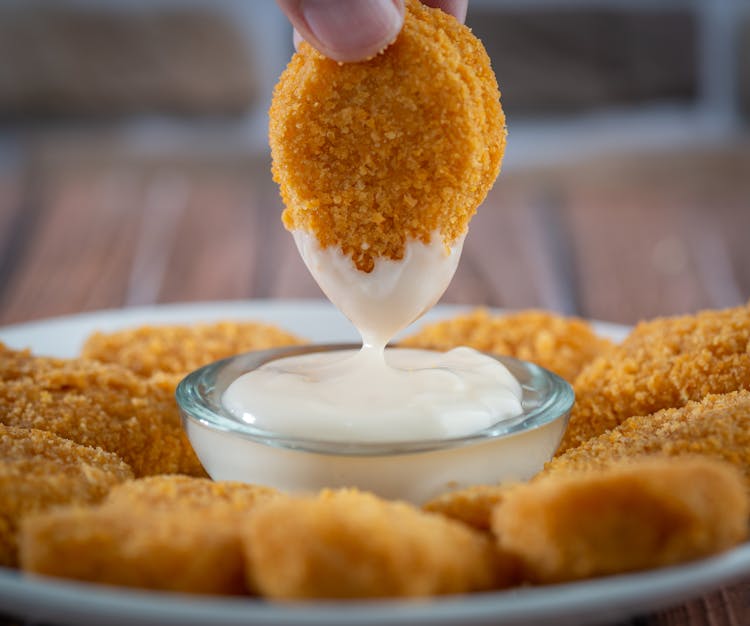 Close-up Of Person Dipping Chicken Nugget In Sauce 