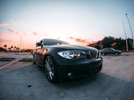 A black BMW sedan parked in an open lot at sunset, captured with a warm glow.