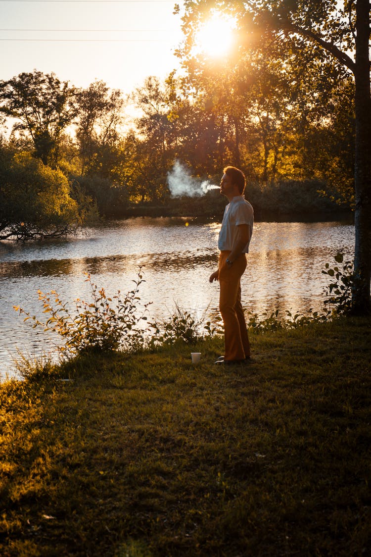 A Man Smoking A Cigarette By The Lake