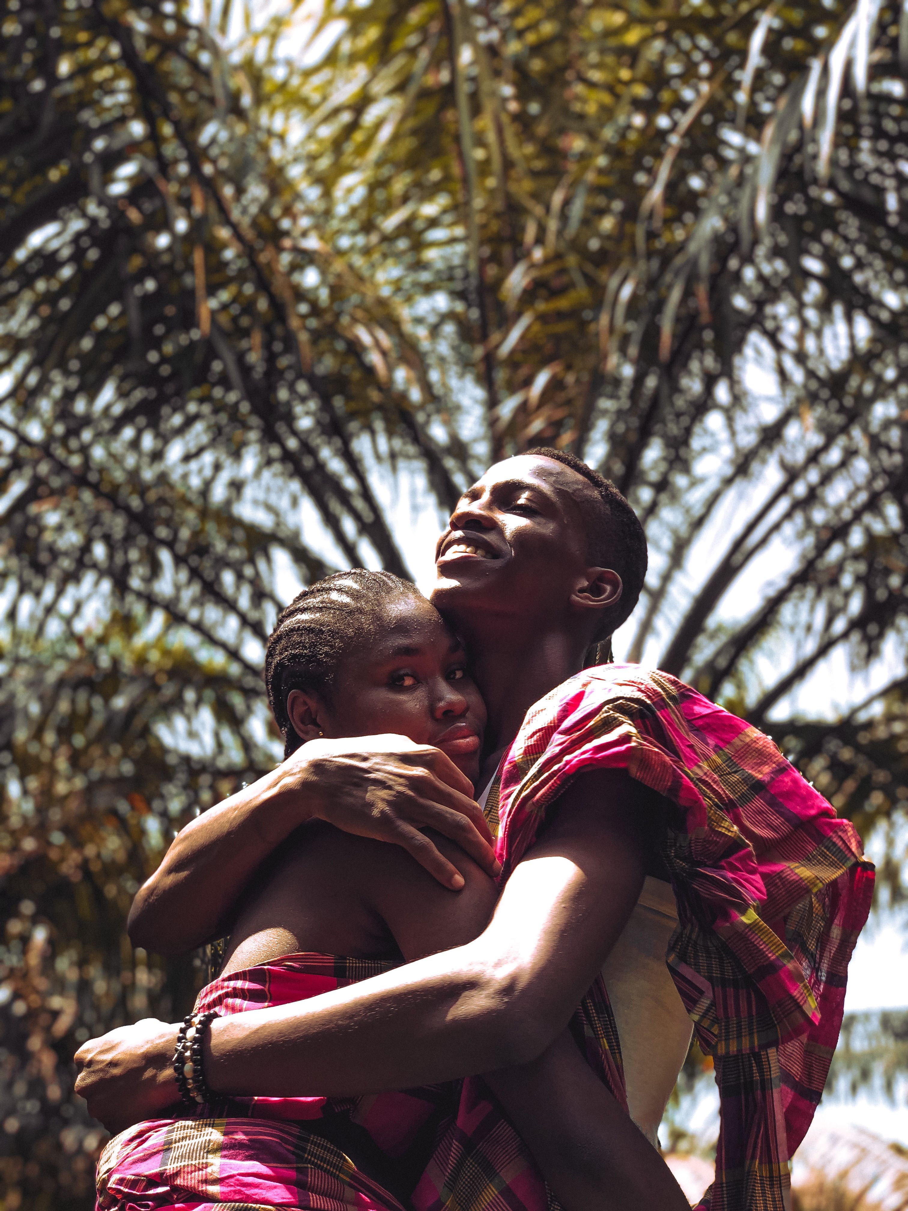 Happy couple embracing outdoors under the sunlight, wearing traditional clothing.