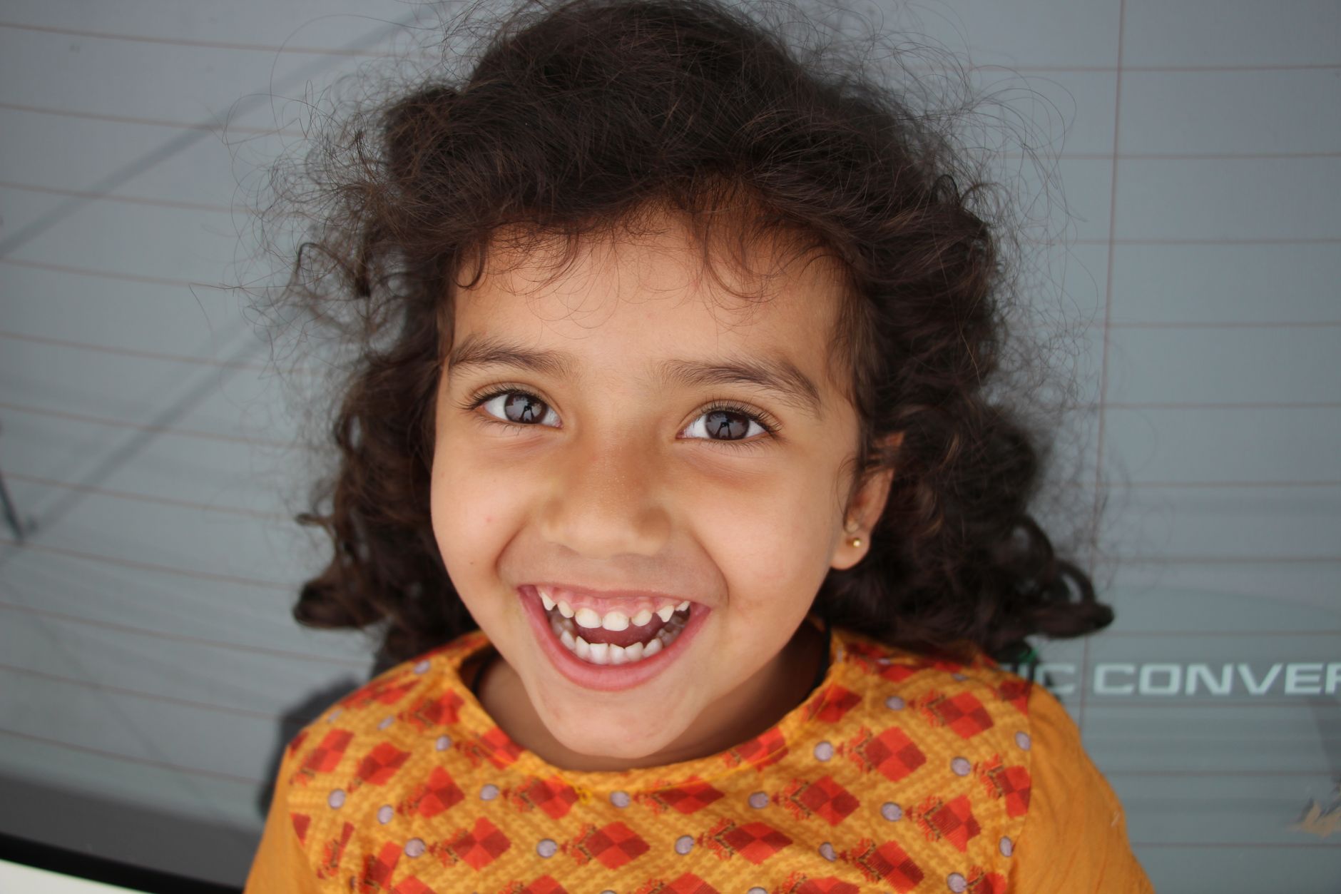 Adorable South Asian girl with curly hair, joyfully smiling outdoors.