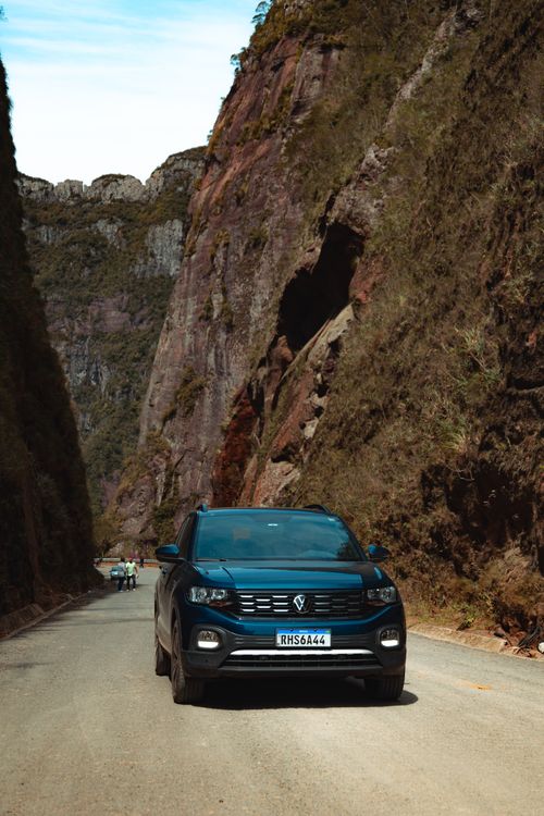 Free Black SUV driving along a road flanked by towering cliffs in a rural mountain setting. Stock Photo
