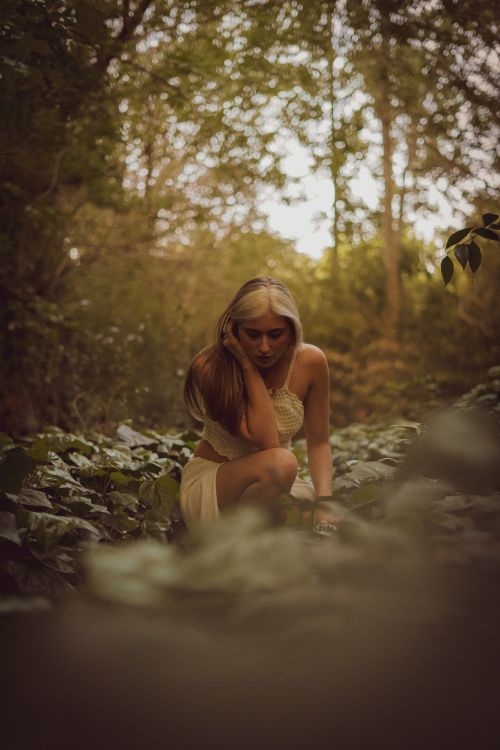 Free A serene portrait of a blonde woman sitting amidst lush greenery in a tranquil forest during summer. Stock Photo