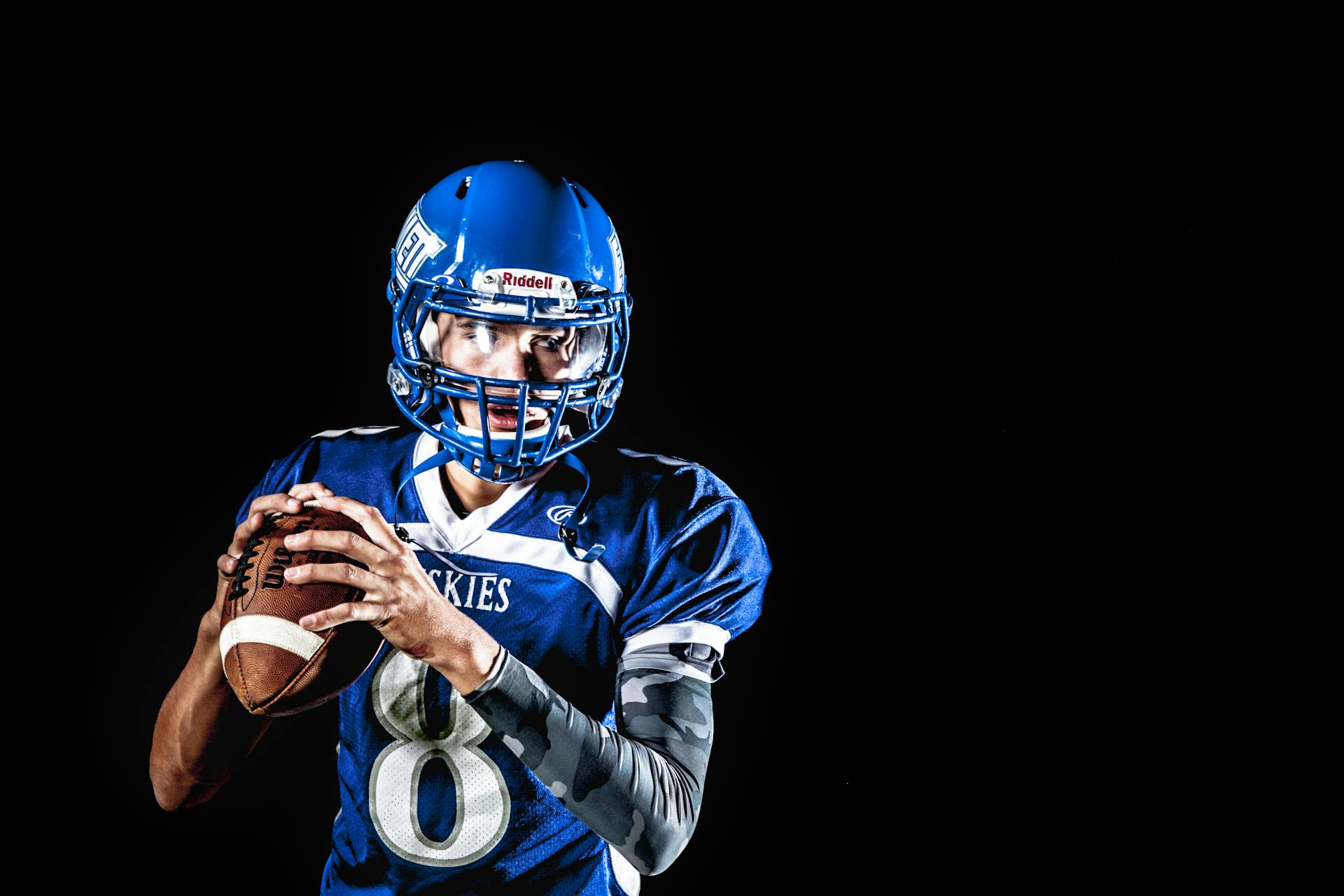 Man Holding Football and Football Uniform in Black Background