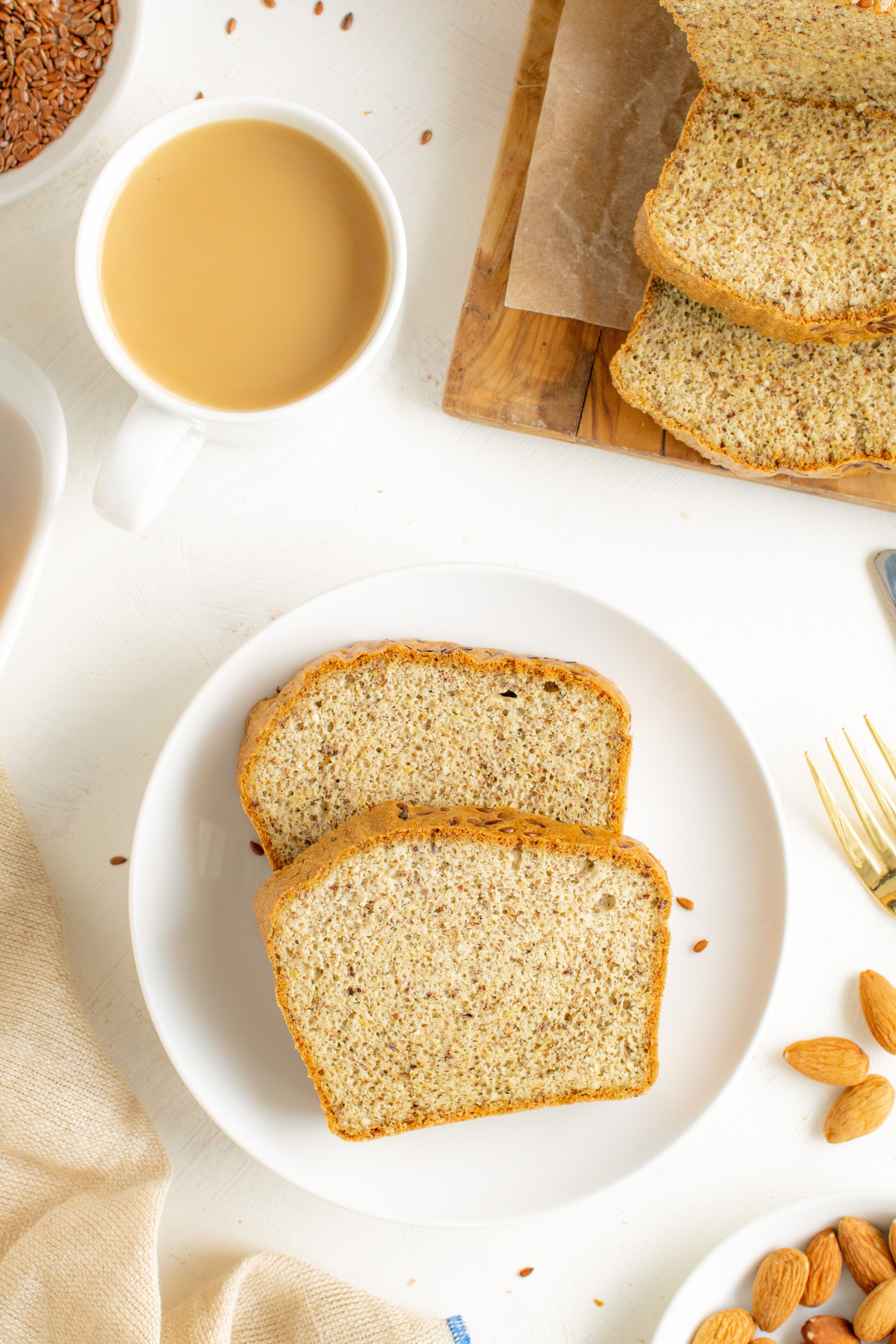 A sliced loaf of grain-free almond flour bread on a wooden board, showing a golden brown crust and a dense, moist, fine-crumbed interior.