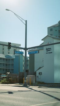 City street intersection with signs and sunlit beach resort, capturing urban coastal life.