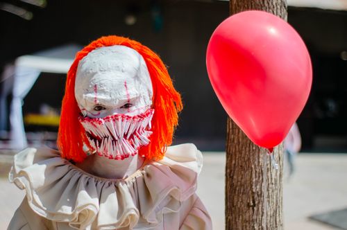 Free A person in a scary clown costume with a red balloon outdoors, perfect for Halloween themes. Stock Photo