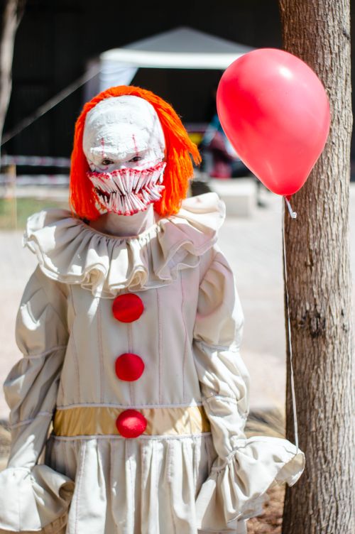 Free A creepy clown in a white costume holds a red balloon outside, creating a chilling atmosphere. Stock Photo