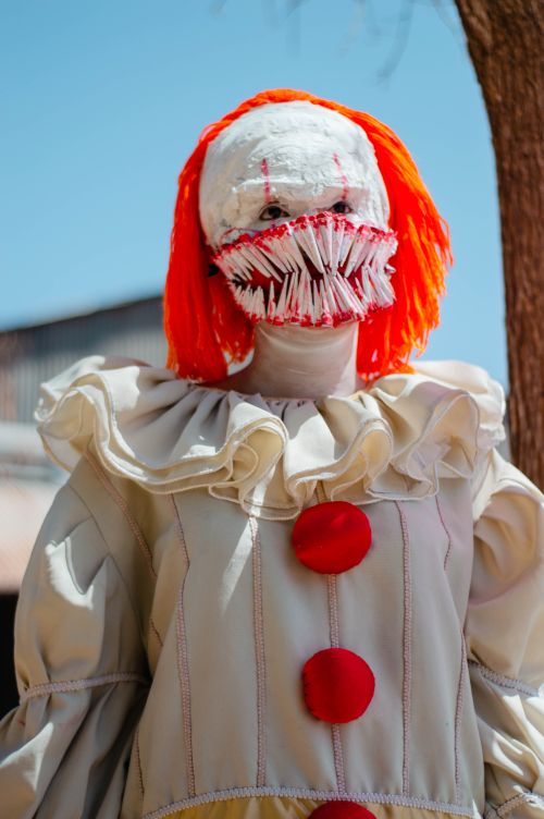 Free An eerie clown in a detailed costume and mask stands brightly under the sun, incorporating horror elements. Stock Photo