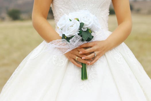 A bride in a white dress holding a bouquet of white roses against an outdoor backdrop, showcasing elegance and charm.