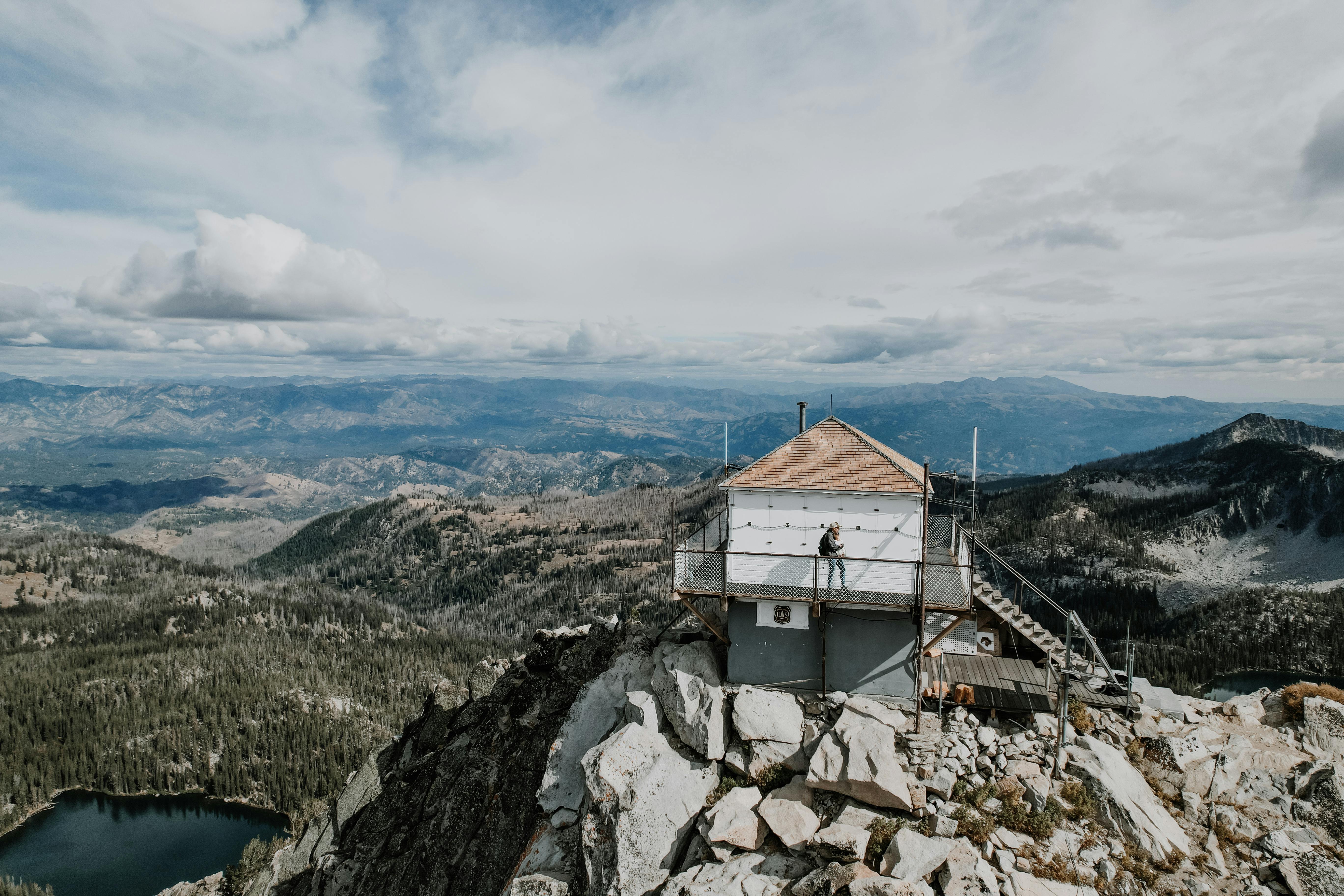 Scenic mountain landscape featuring an elevated cabin with a distant lake view and cloudy skies.