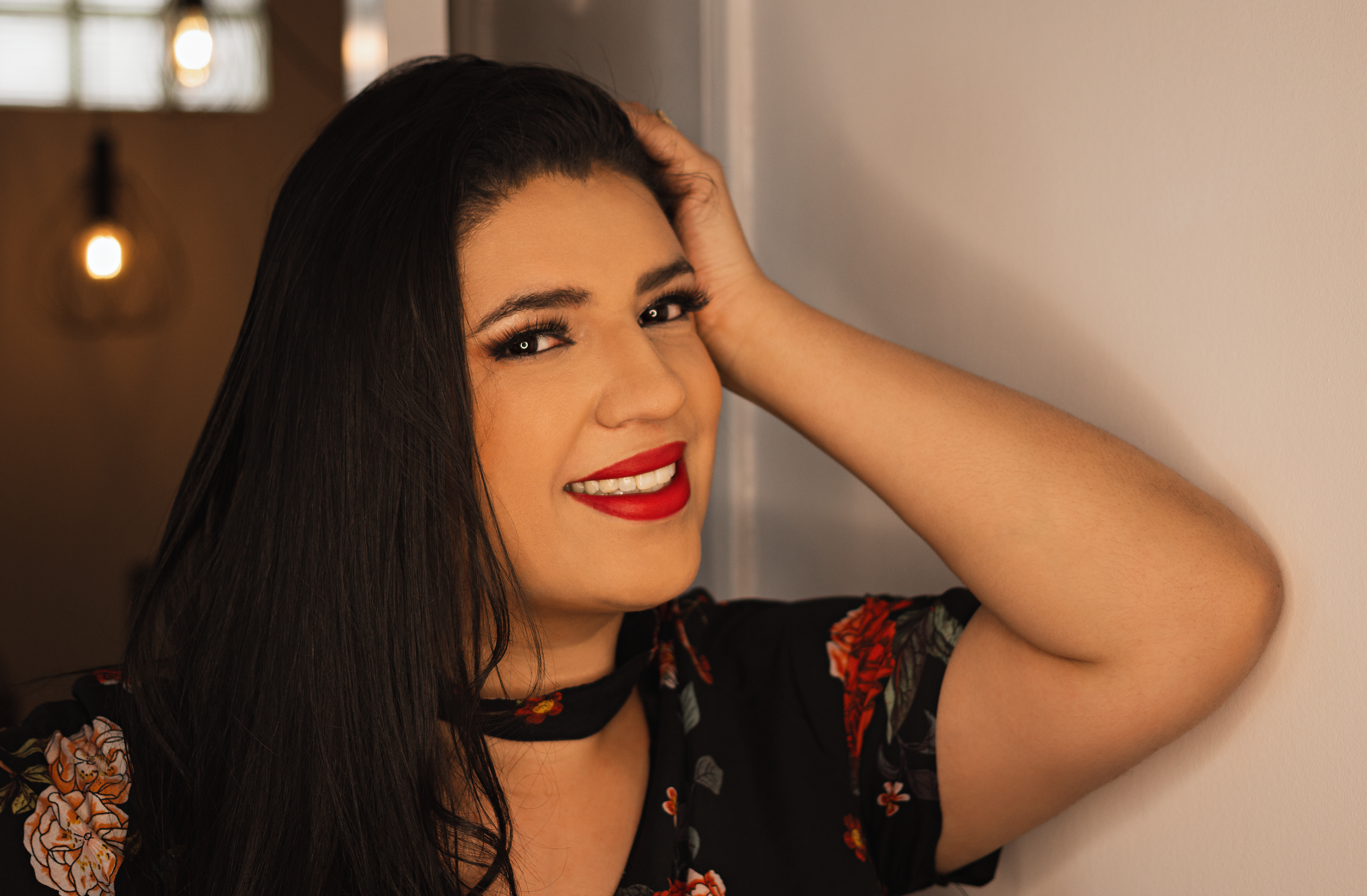 Close-up portrait of a smiling woman with vibrant red lips and floral attire indoors.