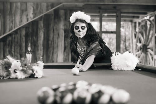 Black and White Photo of a Woman in a Death Mask Playing Billiard