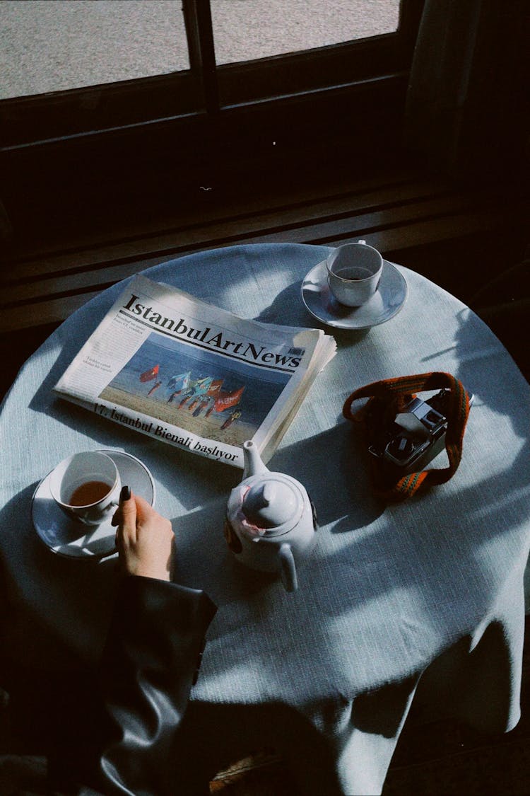 High Angle View Of A Woman Drinking Tea, And Newspaper On A Table