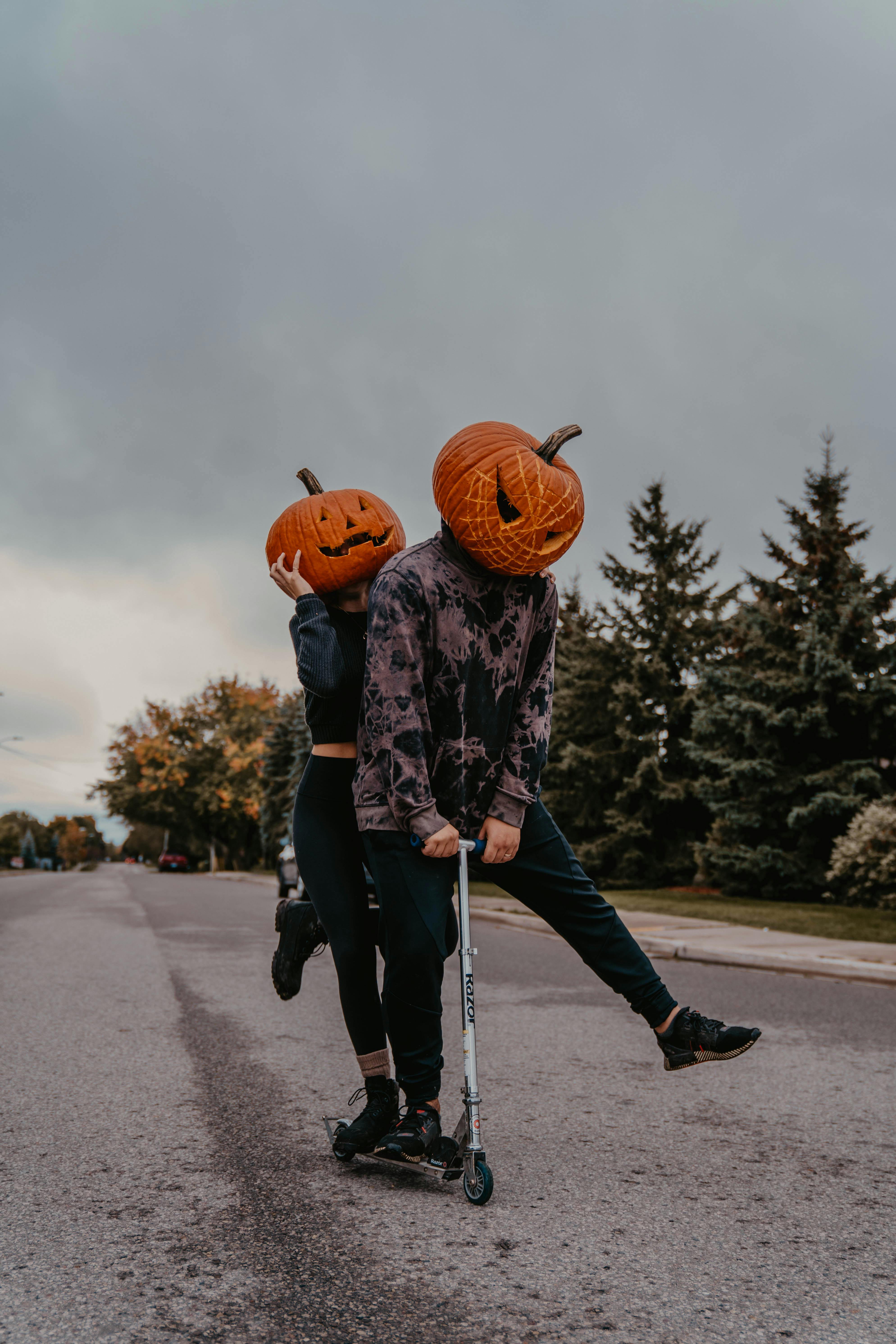 two people with pumpkin headwear riding a scooter