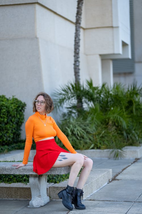 Woman in Orange Long Sleeve Shirt Sitting on Concrete Bench