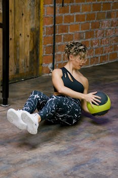 Caucasian woman performing workout with medicine ball in gym setting.