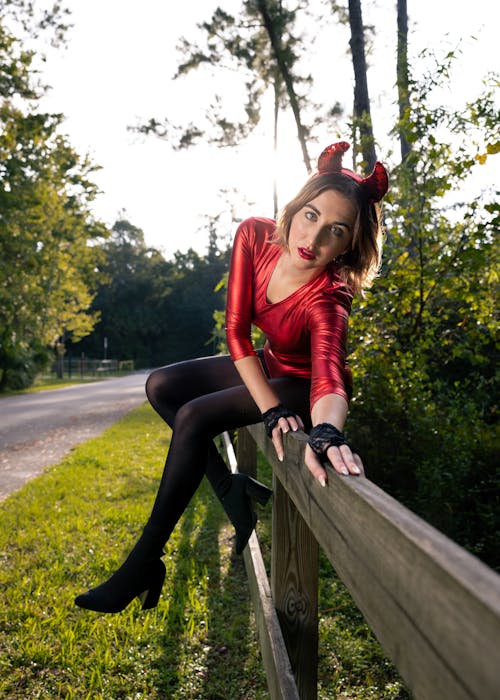 Sexy Woman in Evil Horns Sitting on Fence in Park