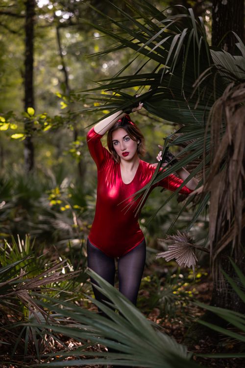 Free A woman in a striking red costume poses amidst lush forest greenery, creating a captivating scene. Stock Photo