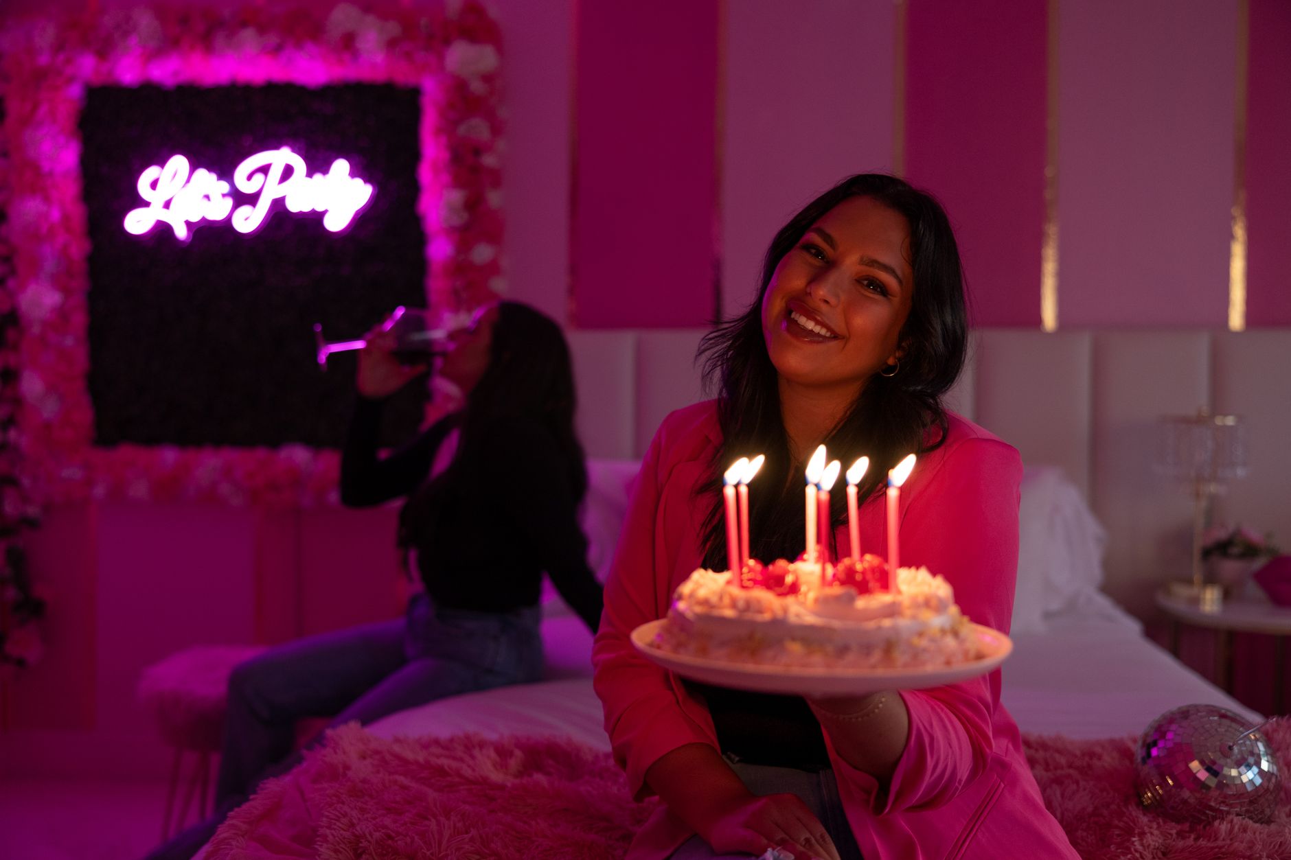 A woman celebrating her birthday with cake and candles in a vibrant pink-themed party setting.