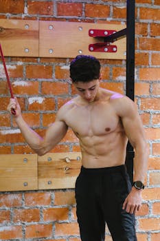 Muscular man exercising shirtless in a Ciudad de México gym with a brick wall backdrop.