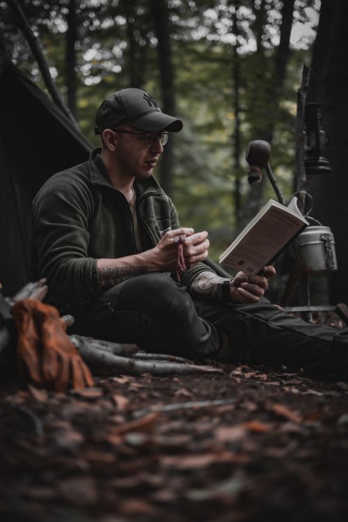 Free Man reading a book while camping in a forest, surrounded by nature. Stock Photo