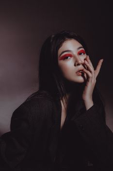 Fashion portrait of a woman with bold pink eye makeup and black clothing in a studio setting.