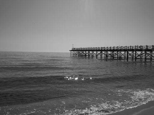 Free Tranquil monochrome image of an ocean pier with gentle waves and sparkling water. Stock Photo